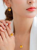 Close-up of a person wearing a gold necklace and earrings with yellow gemstones.