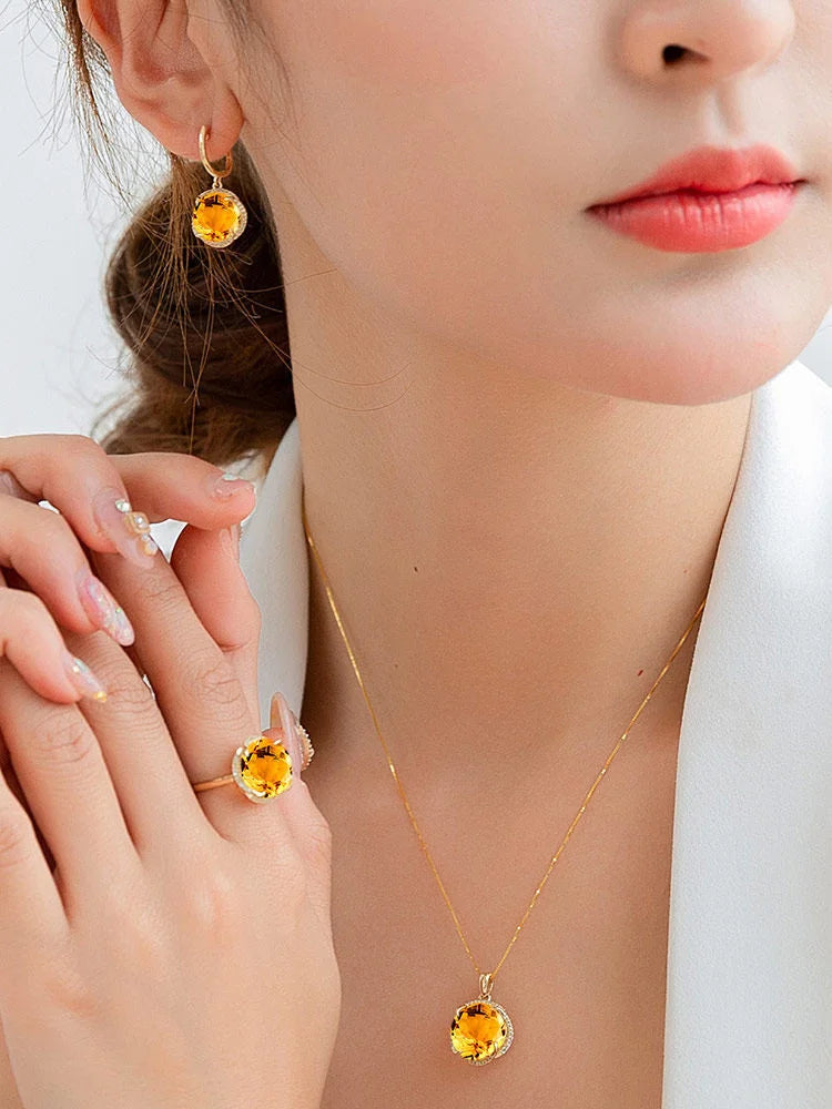 Close-up of a person wearing a gold necklace and earrings with yellow gemstones.