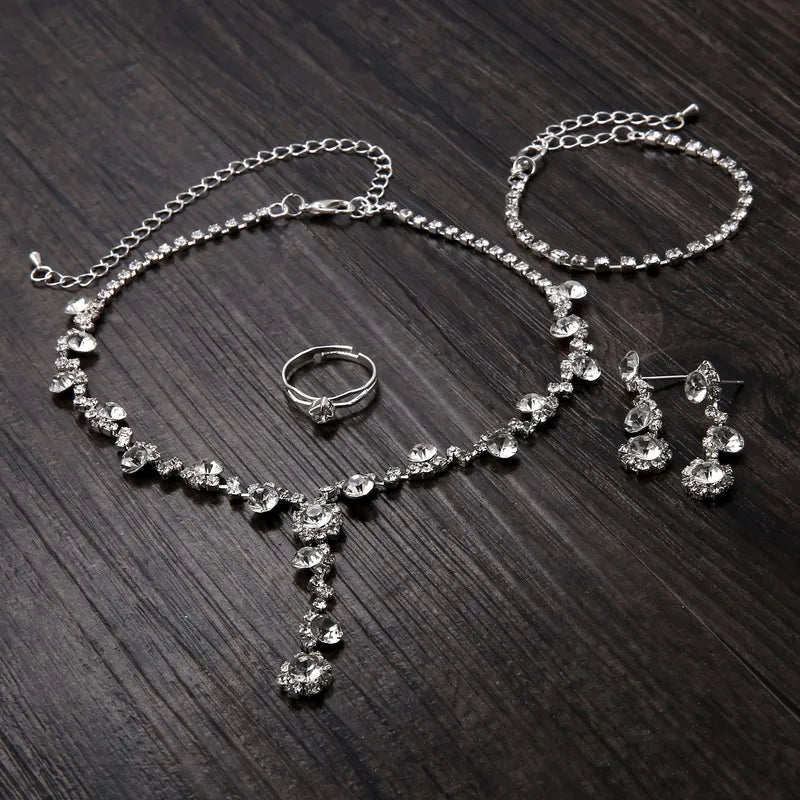 Silver jewelry set with necklace, bracelet, ring, and earrings on a dark wooden surface