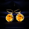 Gold earrings with large orange gemstones on a dark background