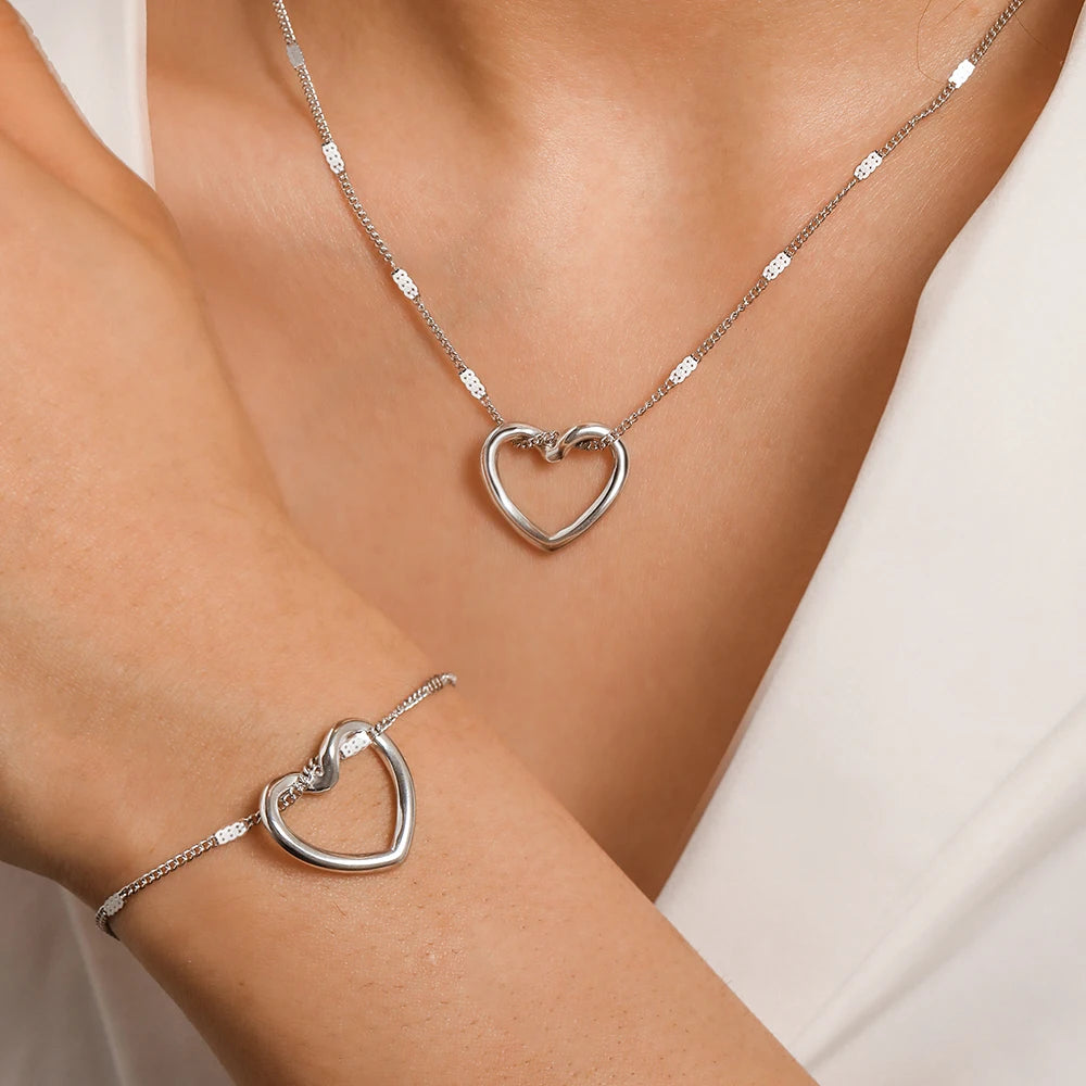 Gold heart-shaped necklace and bracelet on a person wearing a white top.