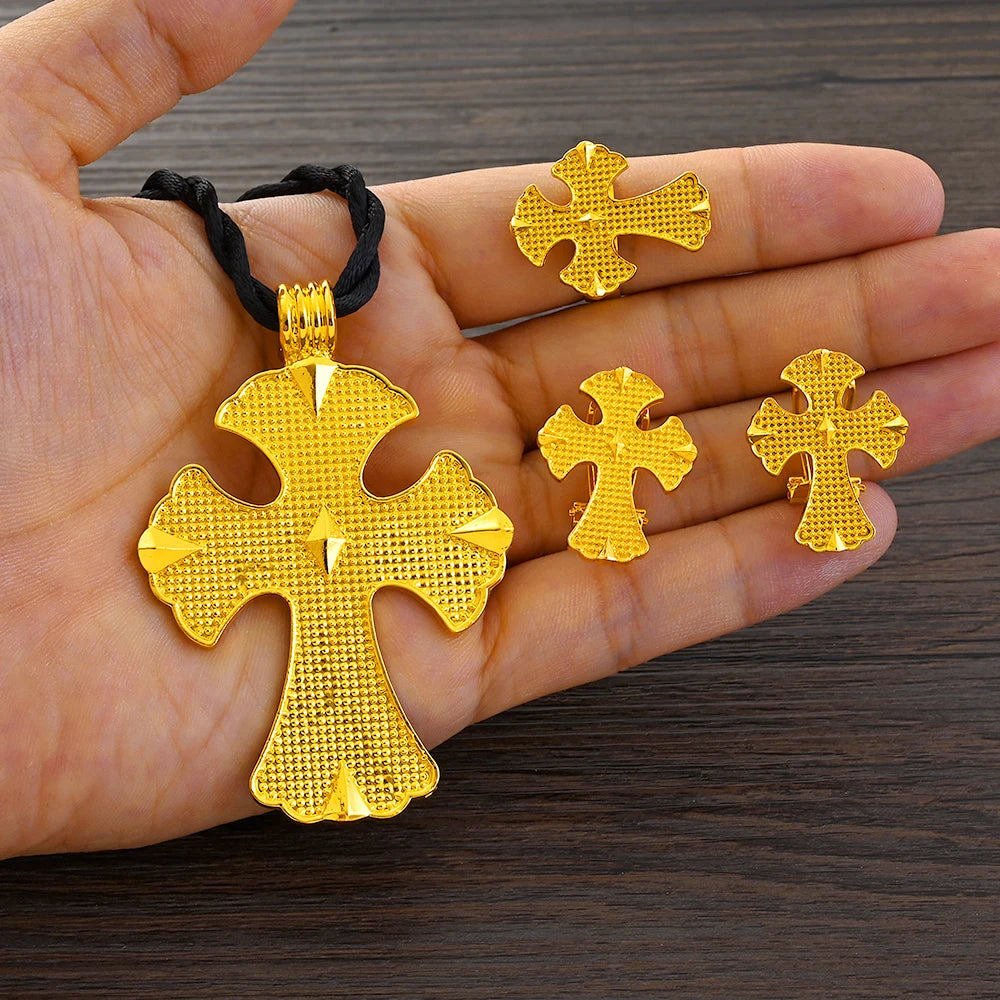 Gold cross-shaped jewelry set held in a hand on a wooden surface