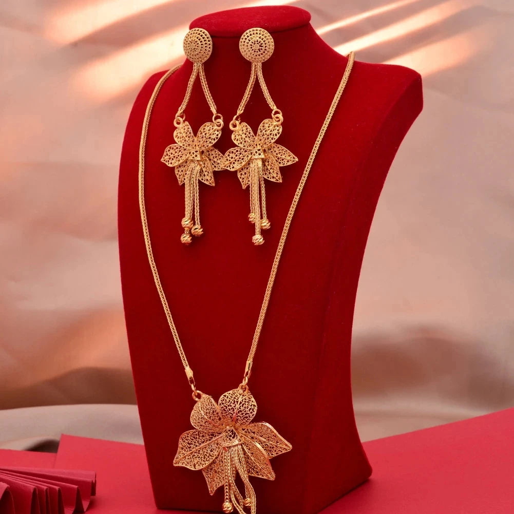Gold necklace and earrings set on a red stand with a soft pink background