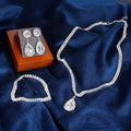 Silver jewelry set including necklace and earrings on a blue fabric background