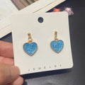 Blue heart-shaped earrings on a jewelry card held by a hand.