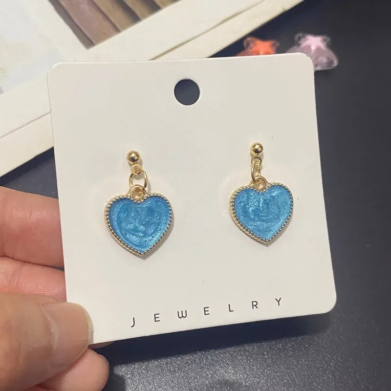 Blue heart-shaped earrings on a jewelry card held by a hand.