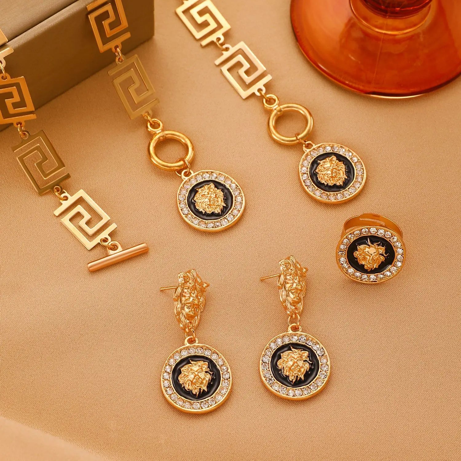 Gold and black lion head earrings on a beige surface