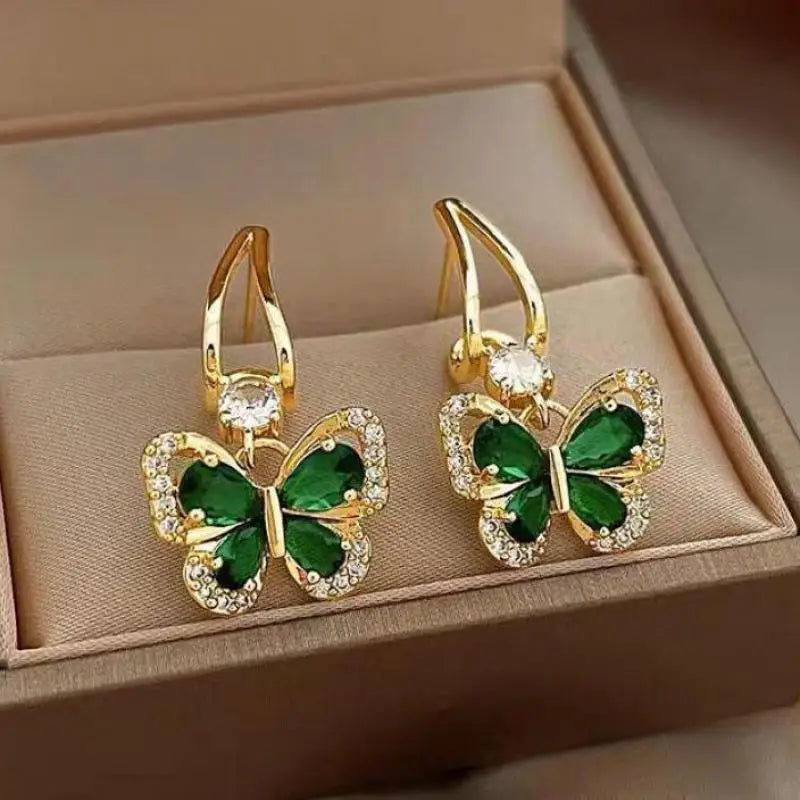 Gold butterfly earrings with green gemstones on a beige jewelry box