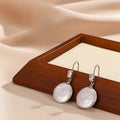 Pearl earrings with silver hooks on a wooden tray with beige fabric background