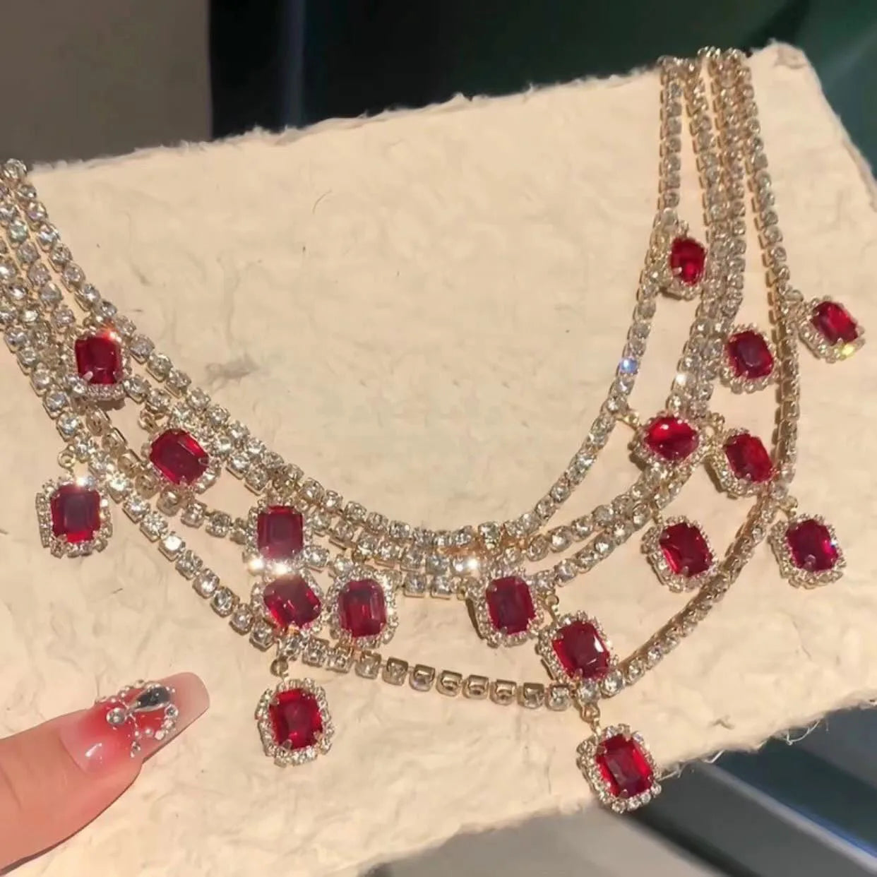 Ornate necklace with red gemstones and a matching earring on a textured surface.