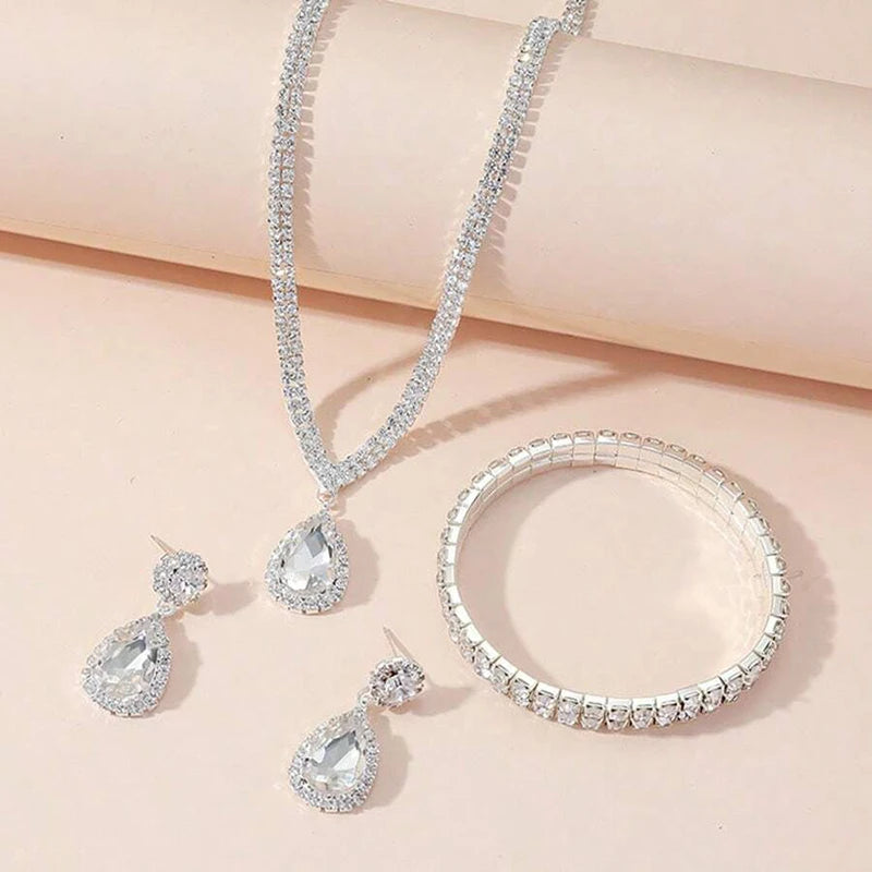 Silver jewelry set with necklace, earrings, and bracelet on a light pink background
