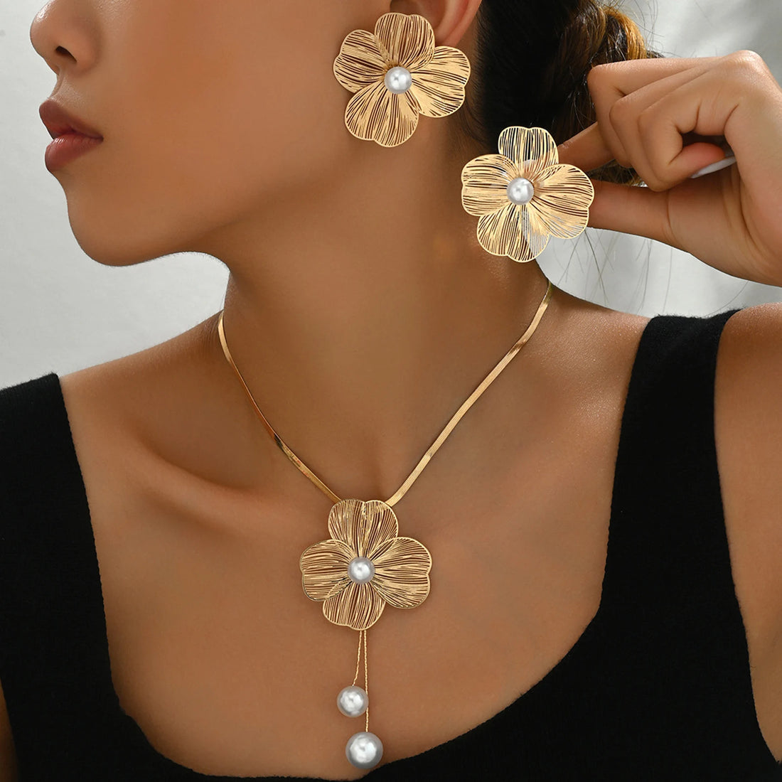 Woman wearing a gold floral necklace and earrings with pearl accents.