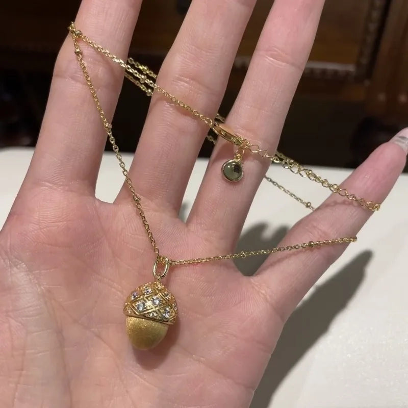 Gold necklace with a pendant on a hand against a neutral background