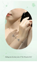 Silver bracelet with heart-shaped charms worn on a wrist, against a light green background.