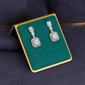 Pair of silver earrings on a green and gold display box against a dark background