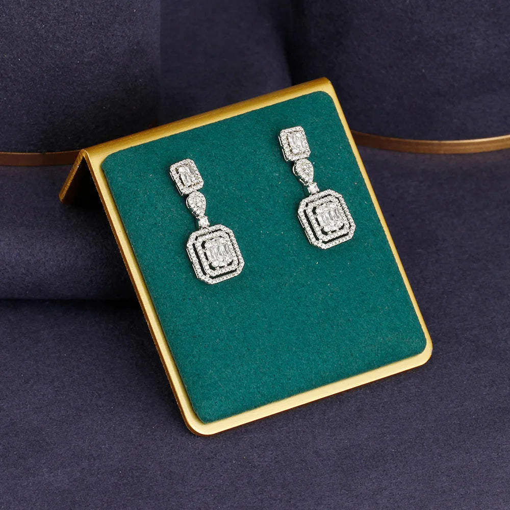 Pair of silver earrings on a green and gold display box against a dark background
