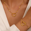 Gold heart-shaped necklace and bracelet on a person wearing a white top.