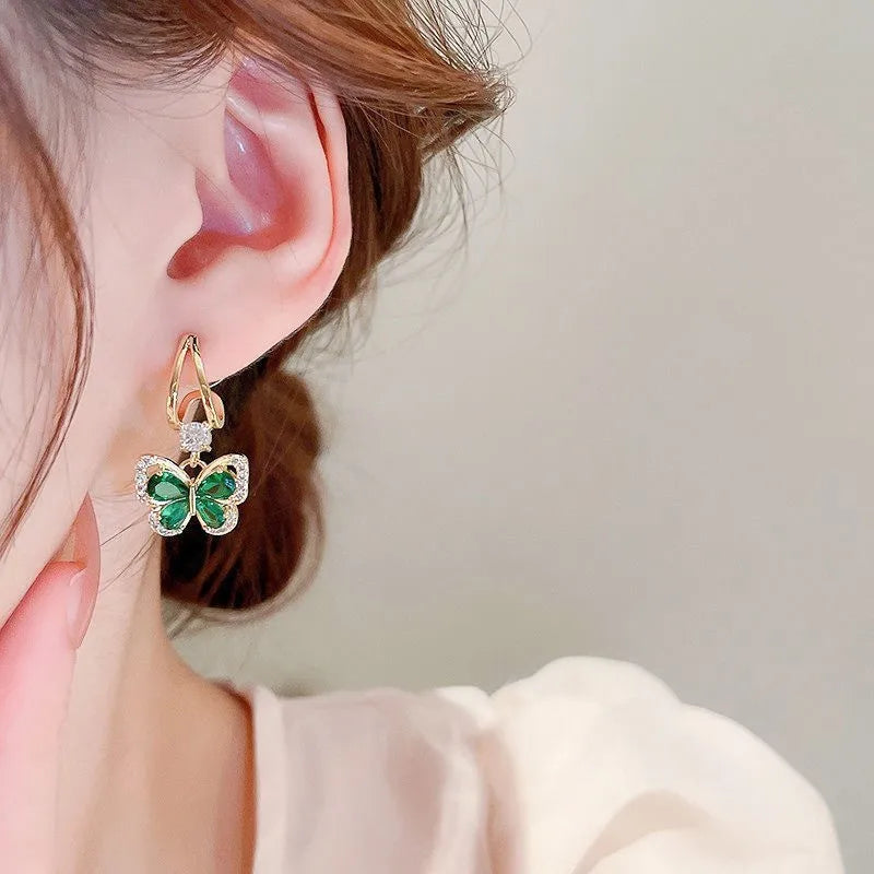 Gold butterfly earrings with green gemstones on a beige jewelry box