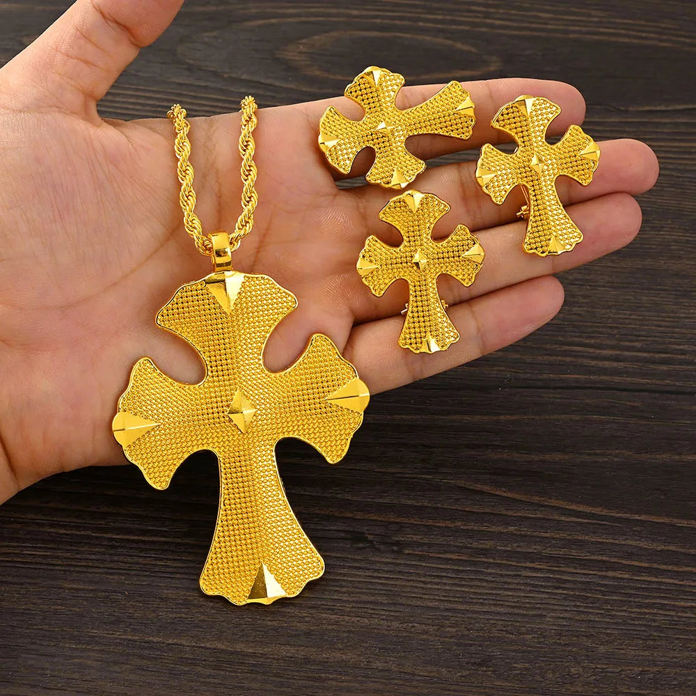 Gold cross-shaped jewelry set held in a hand on a wooden surface