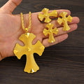 Gold cross-shaped jewelry set held in a hand on a wooden surface