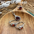 Jewelry set with red gemstones on a wooden surface, including necklace, ring, and earrings.