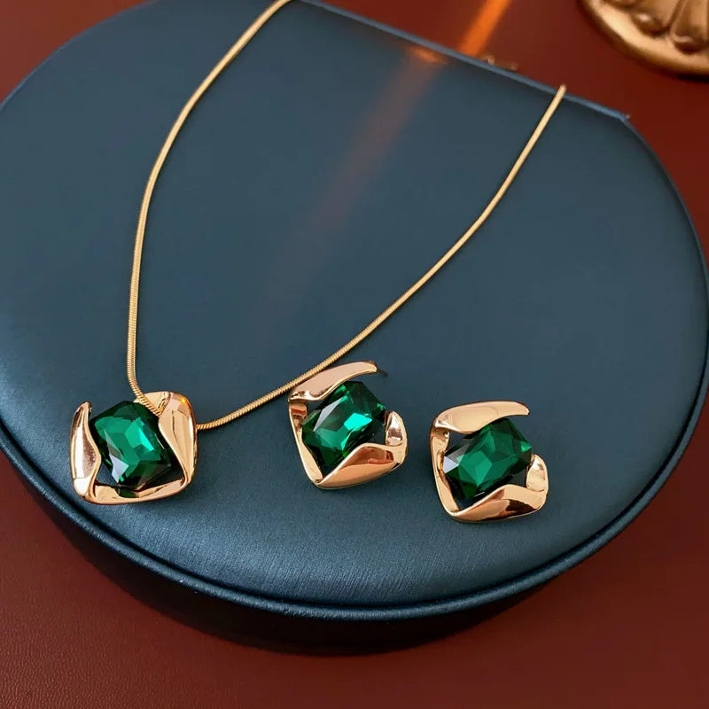 Gold necklace and earrings with green gemstones on a dark blue surface