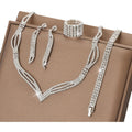 Silver jewelry set including necklace, bracelet, earrings, and ring on a brown surface