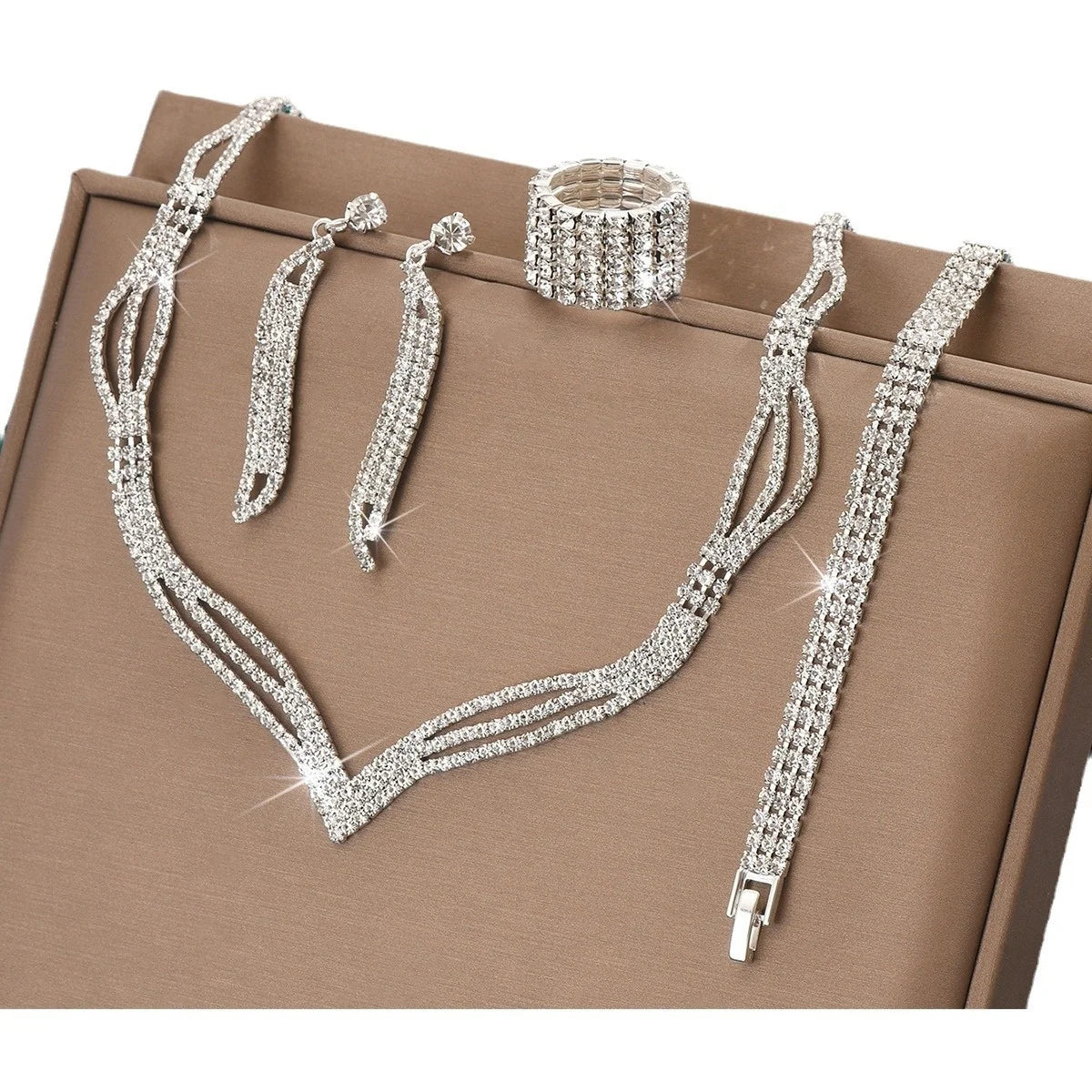 Silver jewelry set including necklace, bracelet, earrings, and ring on a brown surface