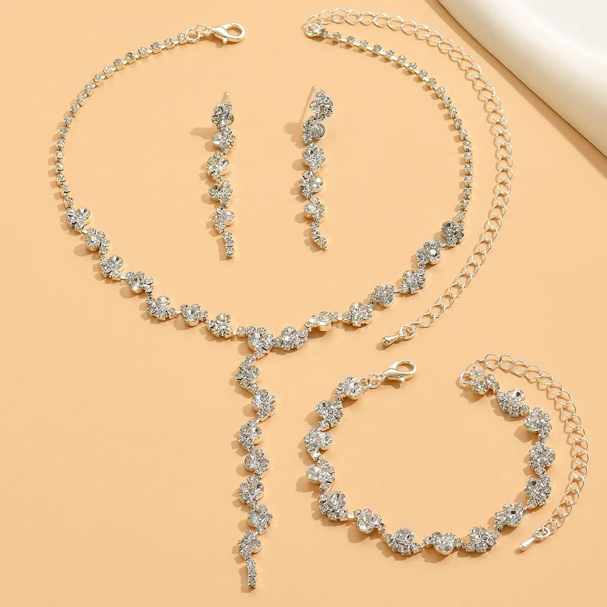 Silver jewelry set with necklace, earrings, and bracelet on a beige background