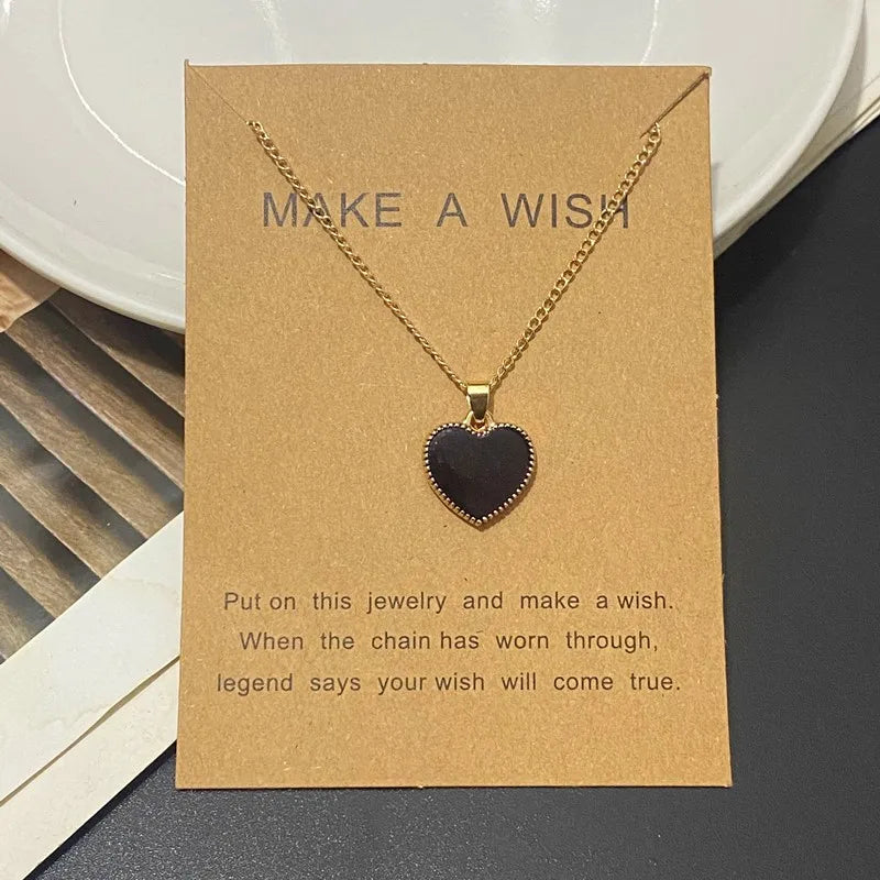 Gold necklace with a black heart pendant on a brown card with text
