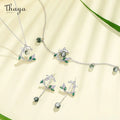 Jewelry set with necklace, earrings, and ring featuring green gemstones on a light background with 'Thaya' branding.