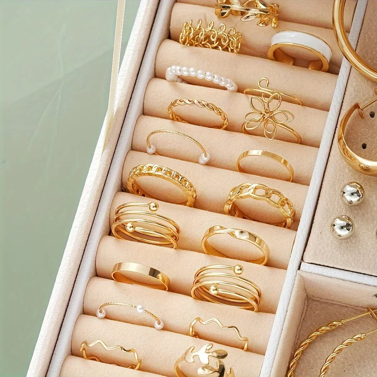Collection of gold rings in a jewelry box on a light green background