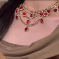 Close-up of a person wearing a luxurious necklace with red gemstones and gold accents.