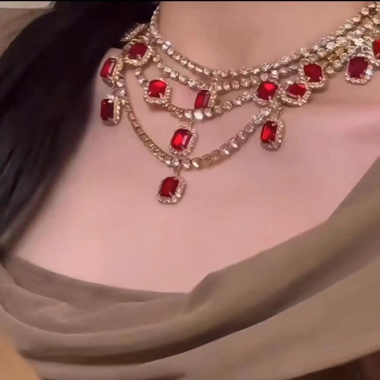 Close-up of a person wearing a luxurious necklace with red gemstones and gold accents.