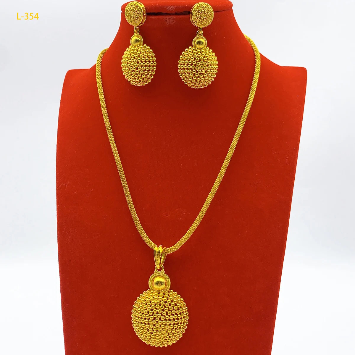 Gold necklace and earrings set on a red stand with a white background