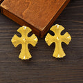 Gold cross-shaped earrings on a wooden surface