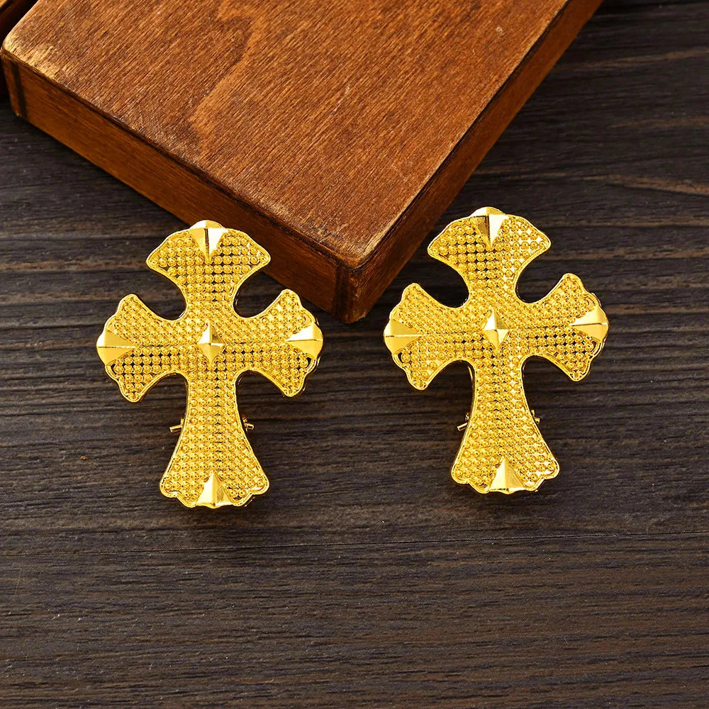Gold cross-shaped earrings on a wooden surface