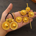 Gold jewelry set including earrings and a hairpin held in a hand on a wooden surface.