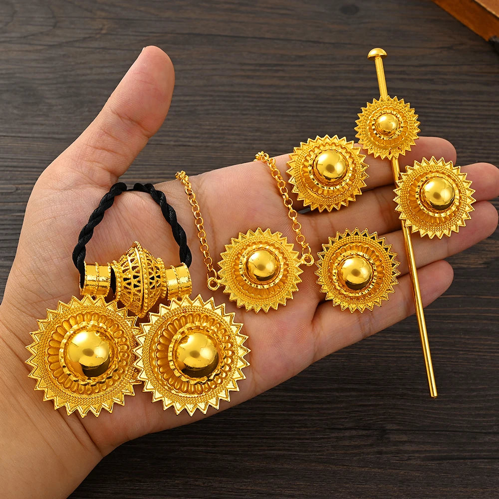 Gold jewelry set including earrings and a hairpin held in a hand on a wooden surface.