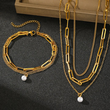 Gold chain bracelet and necklace with pearl pendants on a dark surface