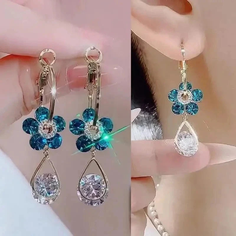 Floral earrings with blue and clear gemstones held by a hand.