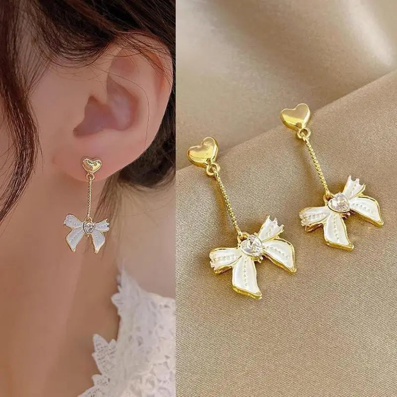 Gold bow-shaped earrings worn by a person, with close-up on ear and side view on beige fabric.