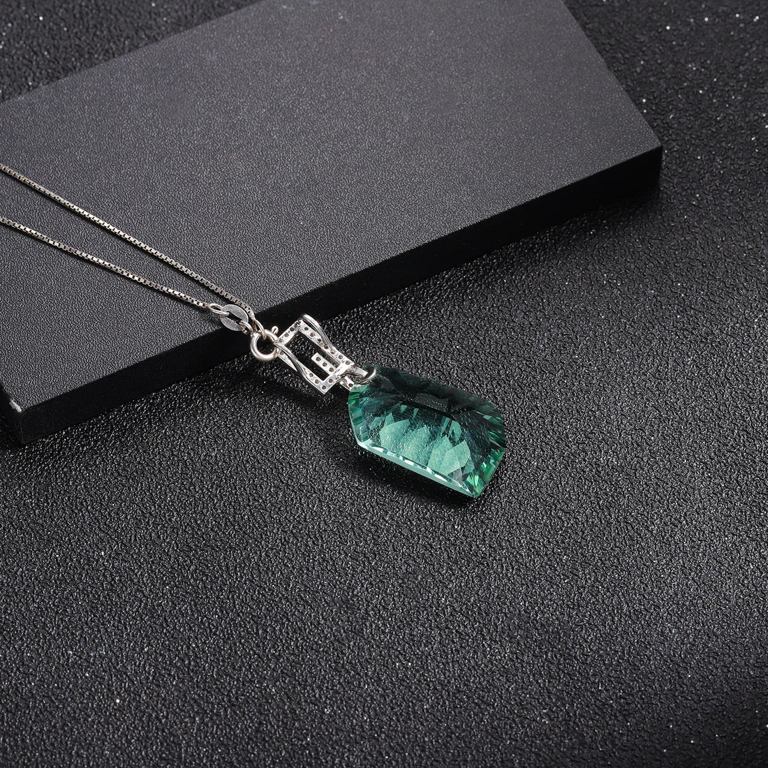 Jewelry set with green gemstones including a ring, earrings, and pendant on a white background.